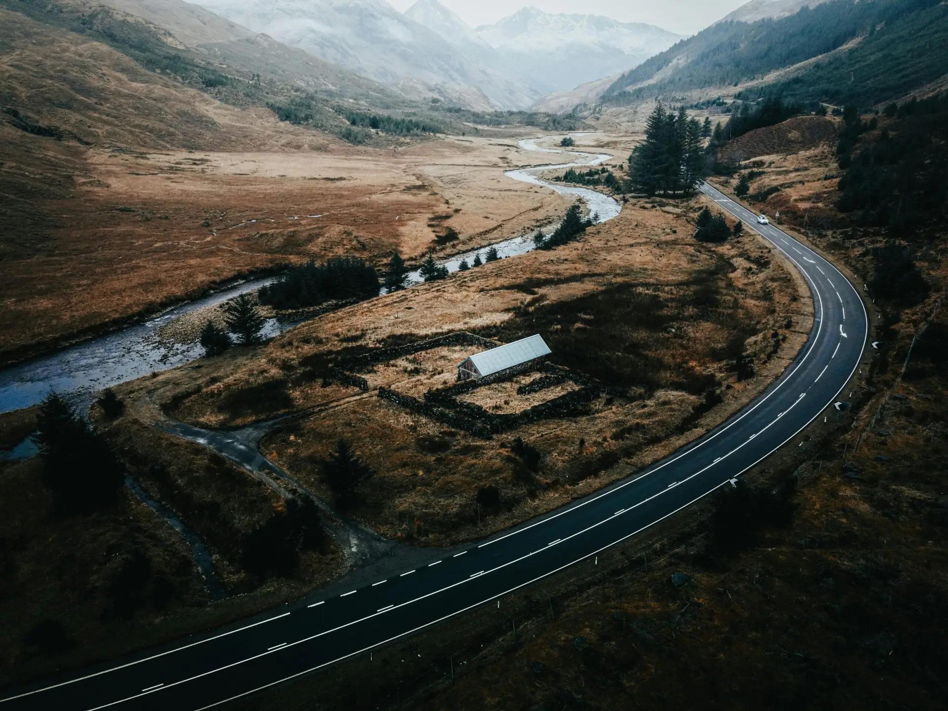 A breathtaking aerial view of a winding road through the Scottish Highlands, with a river and mountains in the background.