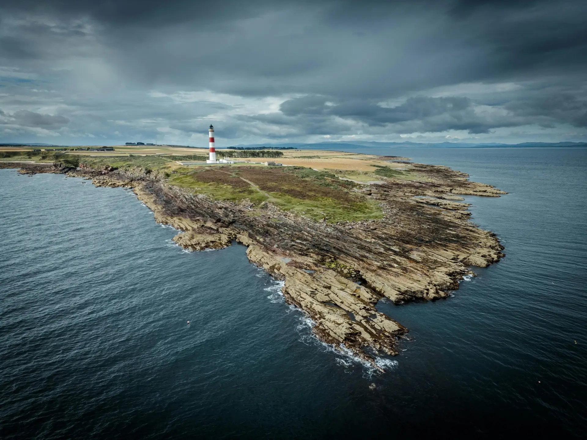 Dramatic aerial view of Duncansby Head lighthouse and rugged coastline in Scotland under stormy skies.